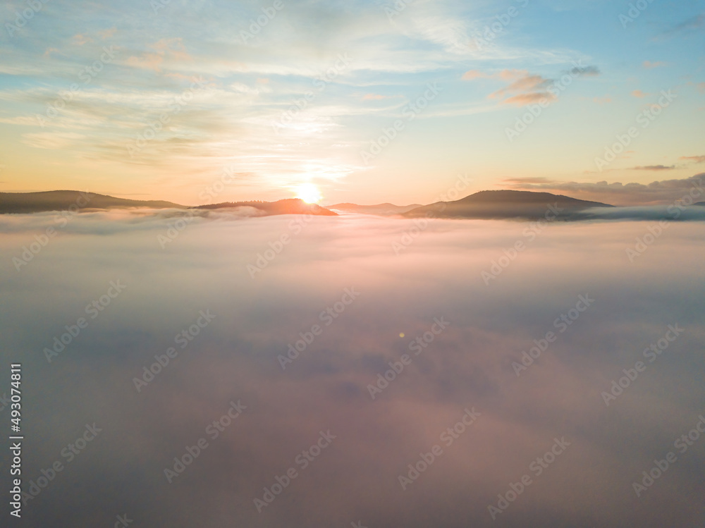 The rays of dawn over the fog in the Ukrainian Carpathians. Aerial drone view.