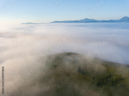 Fog envelops the mountain forest. The rays of the rising sun break through the fog. Aerial drone view. © Sergey