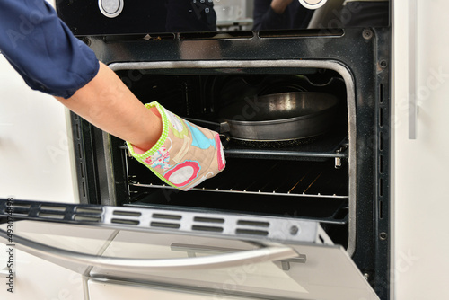A woman in the kitchen in a special mitten opens the hot door to the oven.