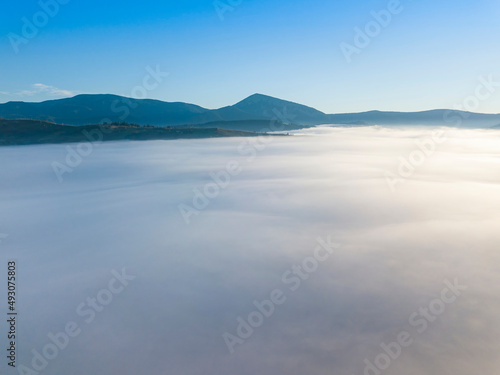 Flight over fog in Ukrainian Carpathians in summer. Mountains on the horizon. A thick layer of fog covers the mountains with a continuous carpet. Aerial drone view.