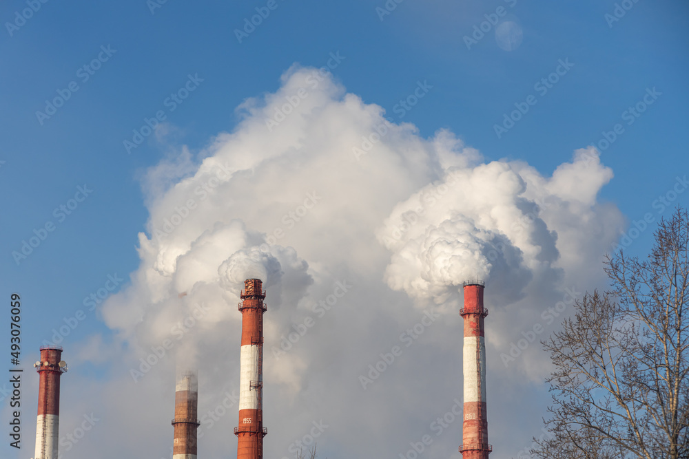 Red and white chimneys of a boiler with smoke against a blue sky in sunny day