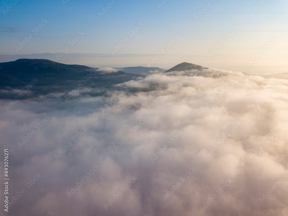 Flight over fog in Ukrainian Carpathians in summer. Mountains on the horizon. Aerial drone view.