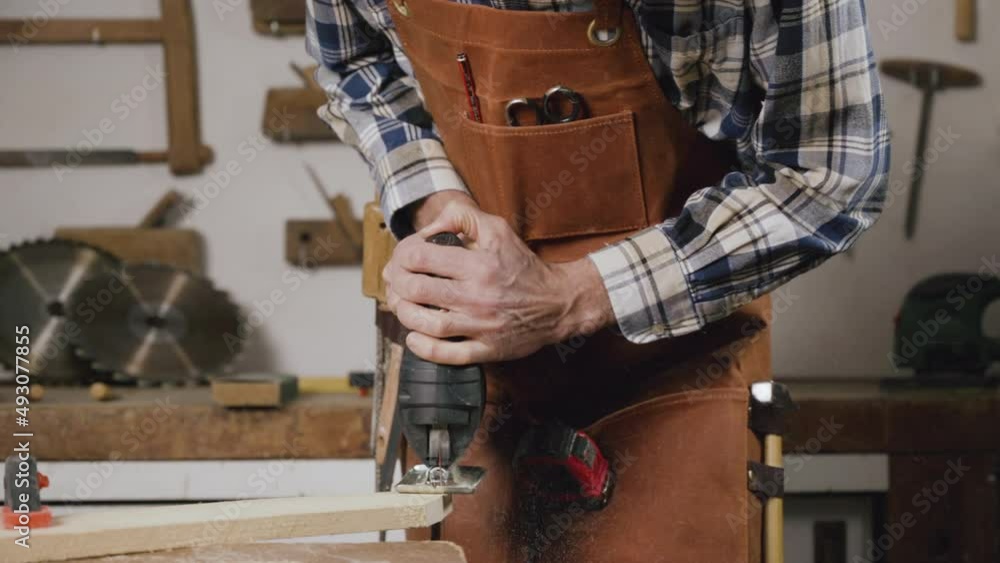 Carpenter is sawing a wood plank with electric jig saw machine in carpentry workshop. Workwood DIY concept. High quality 4k footage Carpenter is sawing a wood plank with electric jig saw machine in carpentry workshop. Workwood DIY concept. High quality 4k footage