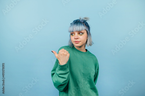 Tableau sur toile Beautiful girl with blue hair and a serious face stands on a blue background and