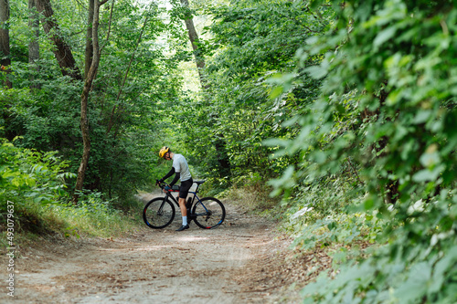 Male cyclist in a full sports outfit with a bicycle trains in nature in a wooded dirt road.