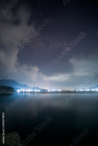 Shining lights reflection at night with stunning stars rises over the lake. Captured at Wadaslintang, Central Java, Indonesia.