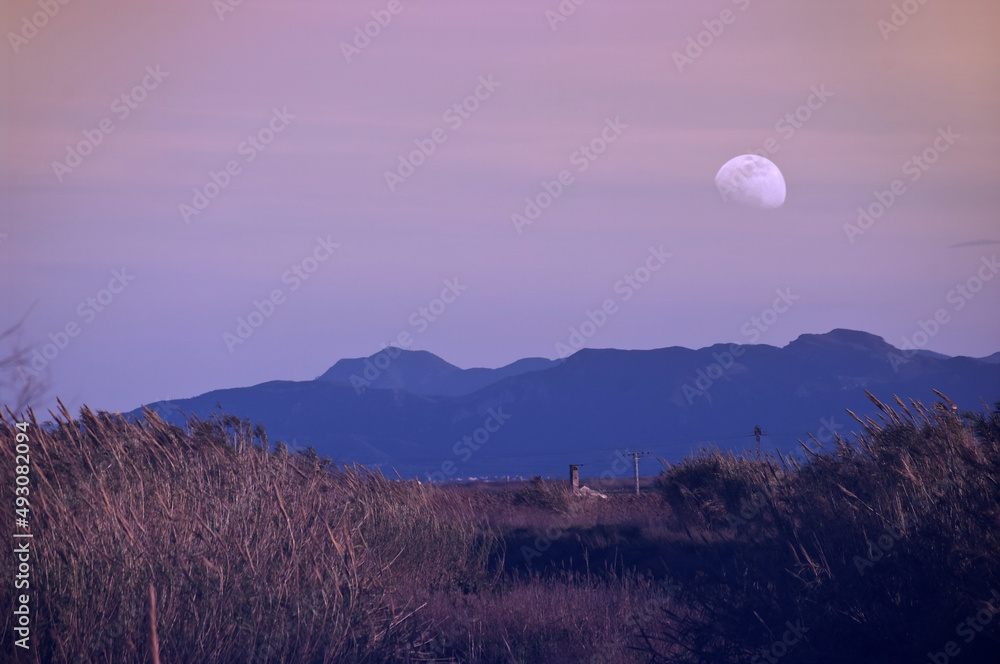 In a sunset, from the mountains the Moon appears in a state of calm.