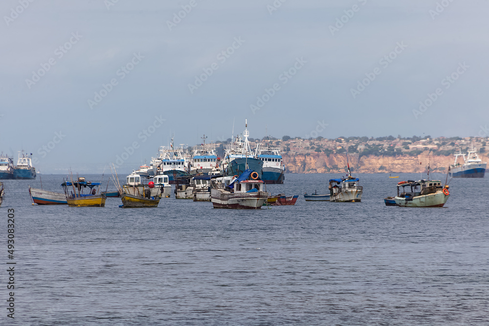 View of fishing boats on the coast of Luanda city, Luanda Bay, with Port of Luanda, transport ships and containers in the background, Angola