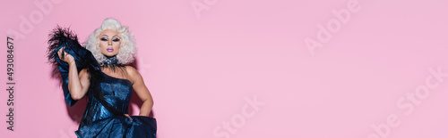 Fotografie glamour drag queen in blue dress looking at camera on pink with copy space, banner