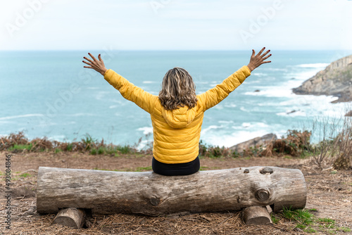 Woman open arms in front of the sea sitting on a log. Powerful woman tasting the freedom and happiness. photo