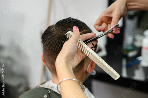 A teenager in a beauty salon gets a haircut, a hairdresser cuts a teenage boy's hair.