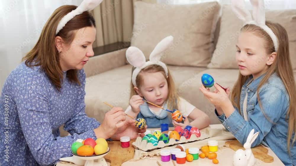 mom and daughters with rabbit ears decorate Easter eggs with paints mom and daughters with rabbit ears decorate Easter eggs with paints