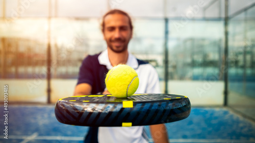 Monitor of padel holding black racket with yellow tennis ball over. Paddel class