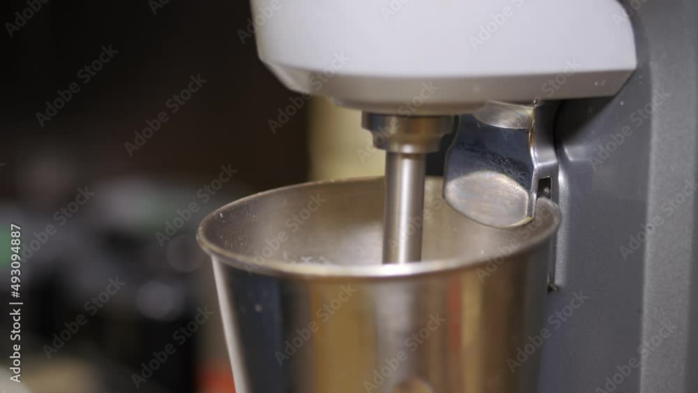 Whipping cream for a coffee cap. A white liquid is automatically whipped in a metal cup with a whisk. Whipping a stable cream cap for a coffee cocktail. Whipping cream for a coffee cap. A white liquid is automatically whipped in a metal cup with a whisk. Whipping a stable cream cap for a coffee cocktail.