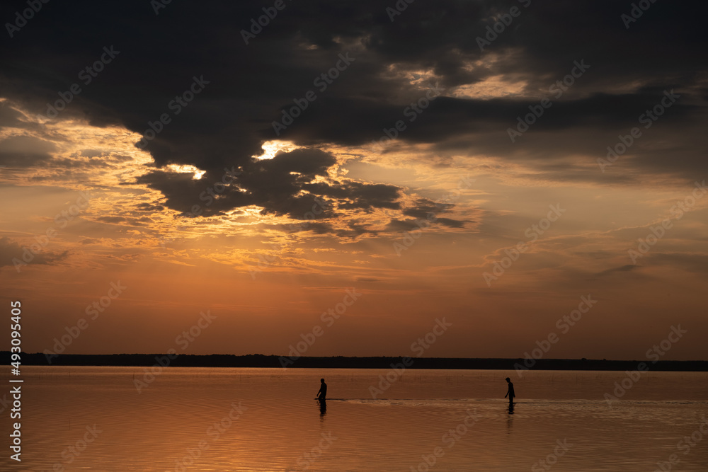 silhouettes of two people walking on water during sunset