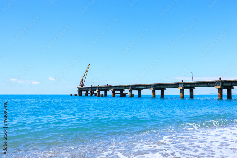 sea coast, blue sea and sky against the backdrop of a pier receding into the distance