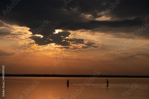 silhouettes of two people walking on water during sunset