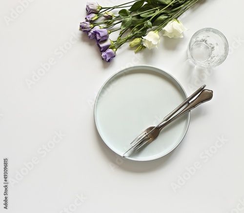 Light blue plate, cutlery and fresh flowers of very peri color on a white background. Flat layot, copy space photo