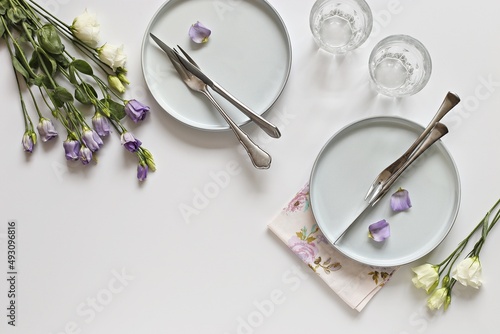 Light blue plate, cutlery and fresh flowers of very peri color on a white background. Flat layot, copy space photo