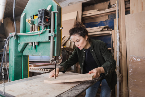 Tableau sur toile Carpenter holding wooden planks near band saw in workshop.