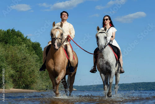 a guy and a girl on horseback on a river on a sunny day