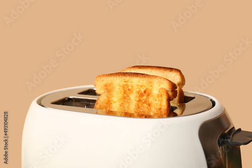 Modern toaster with bread slices on beige background, closeup