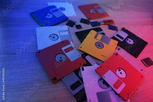 vintage retro electronic data storage devices, from the 80s, 90s flash drives scattered on table. Stack of floppy disks, pendrive and hard disk in grey, black, blue, yellow, red, white, red backlight