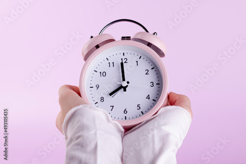 Fotografie Human hands holding pink alarm clock on pink background.