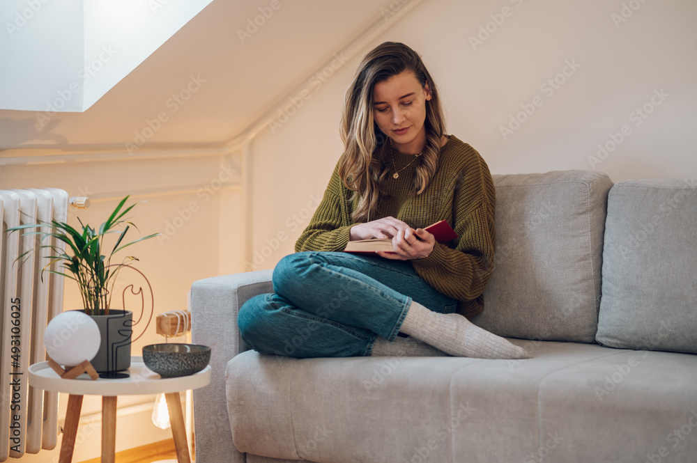 Woman reading a book while sitting on the couch at home Woman reading a book while sitting on the couch at home