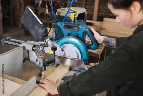 Blurred woodworker using miter saw in workshop.