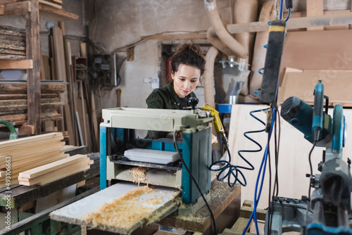 Carpenter working on thickness planer near sawdust in workshop.