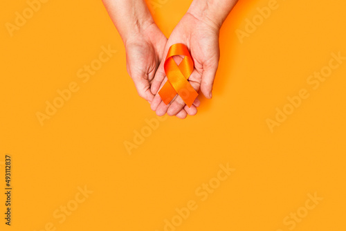 Mano abierta sosteniendo un lazo cinta naranja sobre un fondo anaranjado liso y aislado. Vista superior y de cerca. Copy space photo