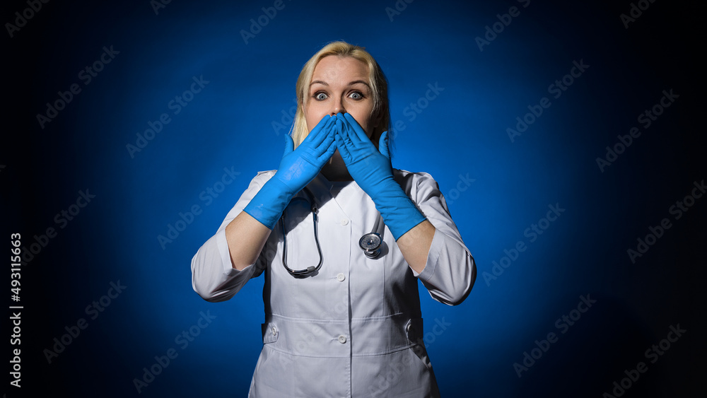 a female doctor in a white coat, gloves, with a stethoscope covered her mouth with her hands on a dark background, the concept is not talking a female doctor in a white coat, gloves, with a stethoscope covered her mouth with her hands on a dark background, the concept is not talking