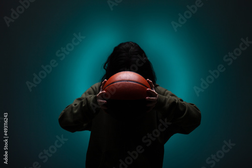 Teenage girl with basketball. Silhouette studio portrait with neon blue colored background.