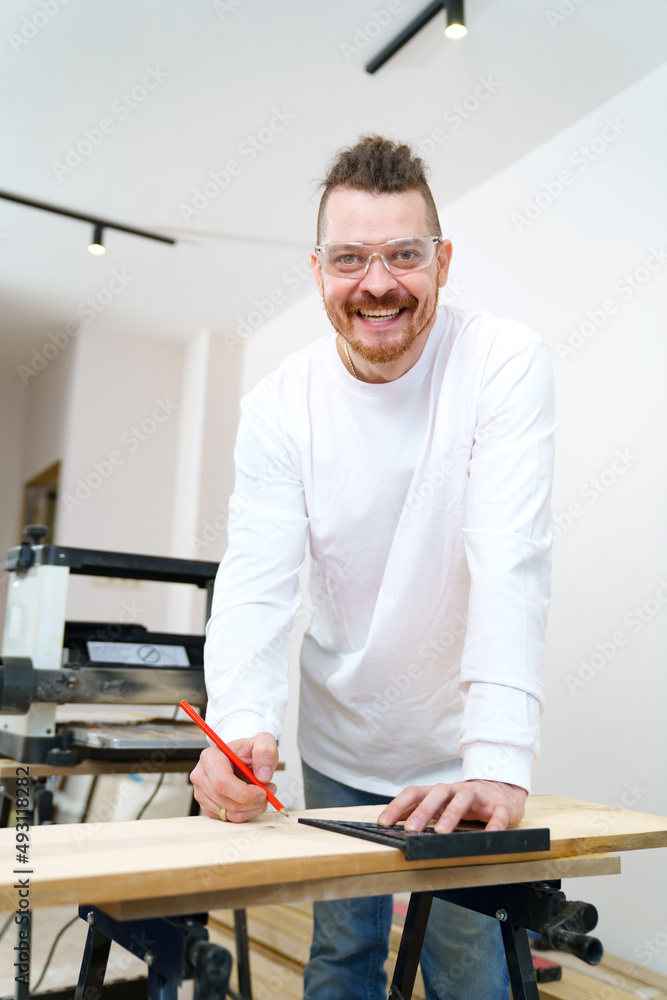 carpenter in protective glasses makes measurements and draws on wood carpenter in protective glasses makes measurements and draws on wood