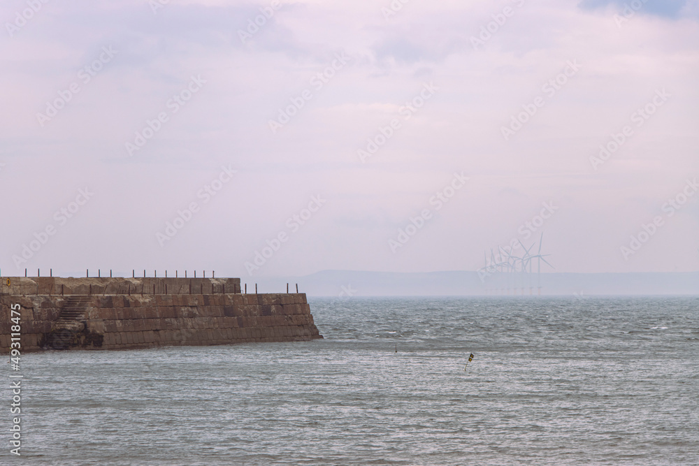 Heugh breakwater pier in stormy, cloudy weather with wind farm behind Heugh breakwater pier in stormy, cloudy weather with wind farm behind