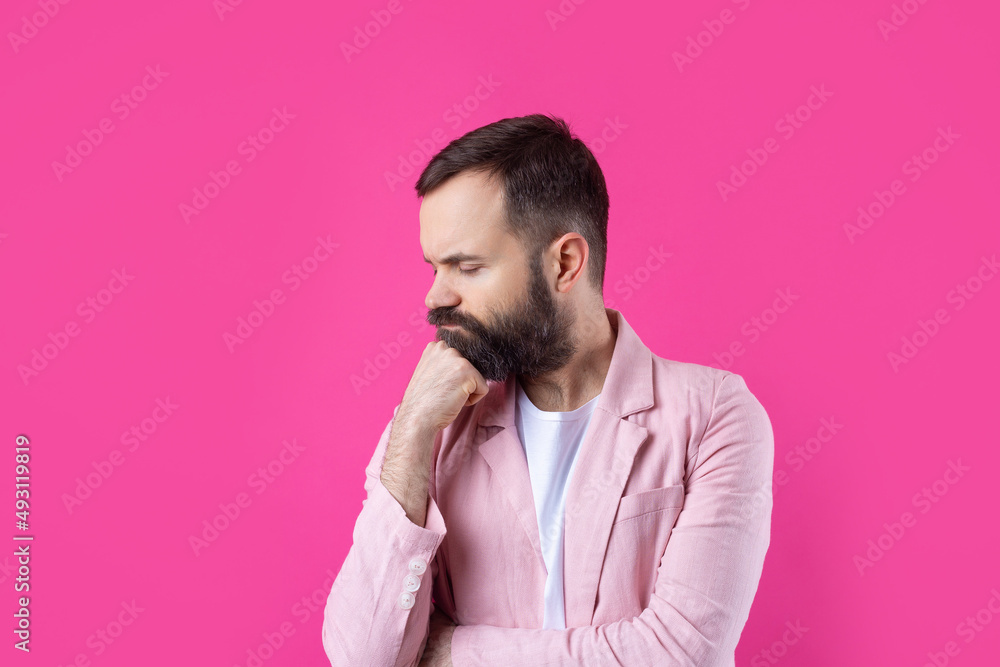 Handsome man with a beard in a pink jacket is thinking over an isolated red background. Handsome man with a beard in a pink jacket is thinking over an isolated red background.