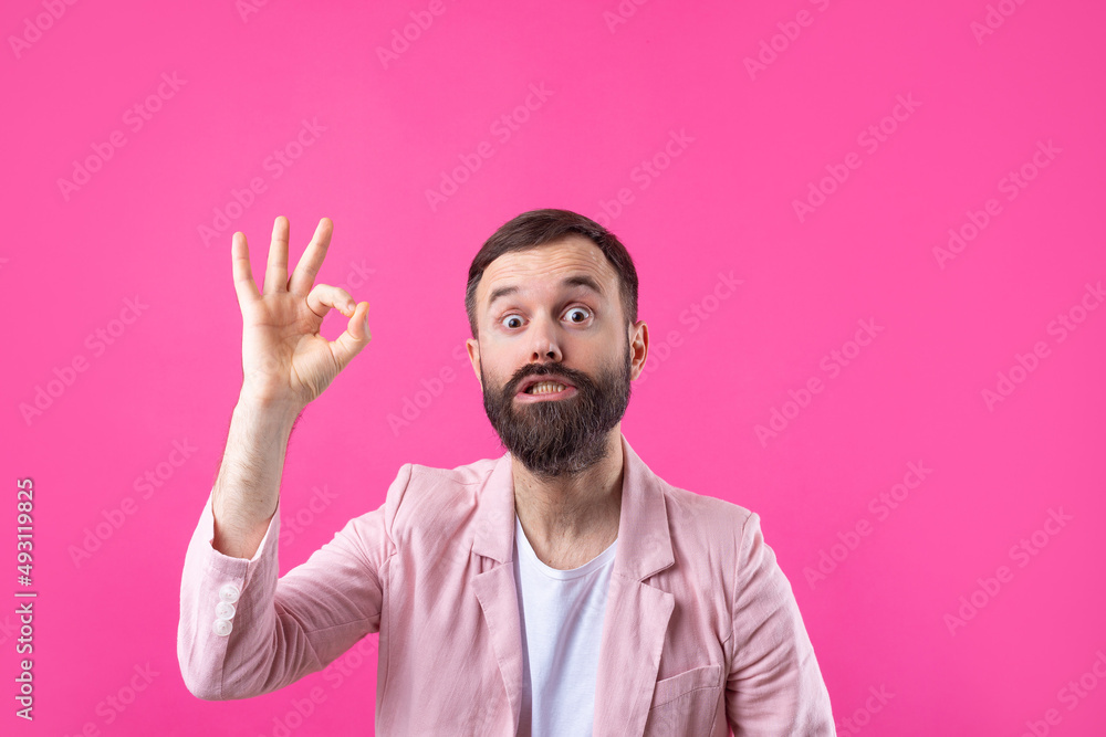 Portrait of a smiling young man in a pink jacket. Man showing ok gesture while standing in studio over isolated red background. Portrait of a smiling young man in a pink jacket. Man showing ok gesture while standing in studio over isolated red background.