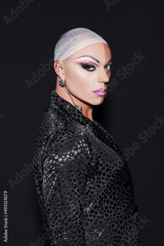 man with piercing and makeup on half face looking at camera isolated on black.