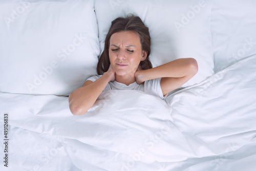 Woman in bed suffering from neck pain in the morning after sleeping on uncomfortable pillow. Pain in neck, cervical chondrosis or osteochondrosis