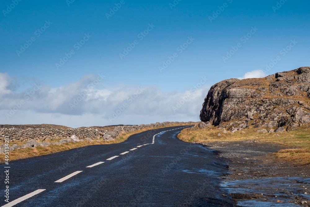 Asphalt road and stone wall, Burren, Ireland. Warm sunny day with cloudy blue sky. Travel and tourism concept