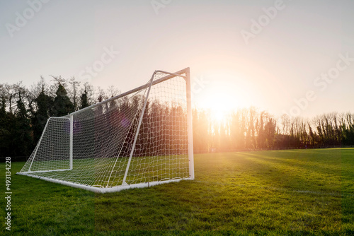 Football or soccer goal post on a green grass pitch in a park at sunset time. Nobody. Calm mood. Sun flare. Sport theme background photo