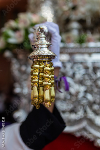 Detail of the hand of a penitent of the brotherhood of the lanzada holding the paso of the virgin in a procession of holy week in granada. Gold thread on an out of focus object.