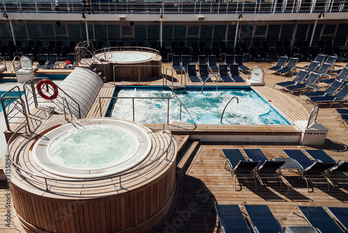 View of a swimming pool and jacuzzi of a cruise ship with no people on board. Deck of a luxury ship with chairs for sunbathing. . High quality photo horizontal
