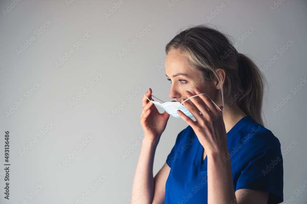 Young pensive caucasian female surgeon putting on or taking off her face mask. High quality photo Young pensive caucasian female surgeon putting on or taking off her face mask. High quality photo