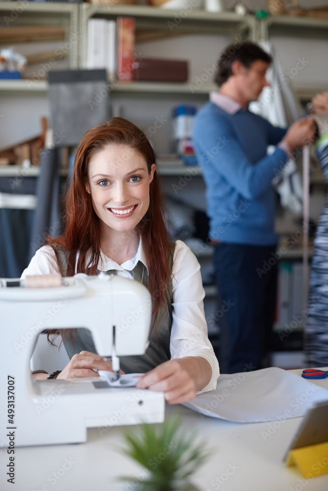 Stitching it all together. Portrait of a young fashion designer sewing while a colleague works in the background. Stitching it all together. Portrait of a young fashion designer sewing while a colleague works in the background.