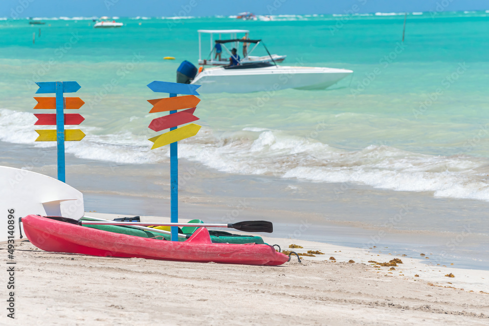 Kayaks on the sand of a beautiful beach and multiple colored signposts. No writing on signposts. Photo taken in Maragogi - AL, Brazil.