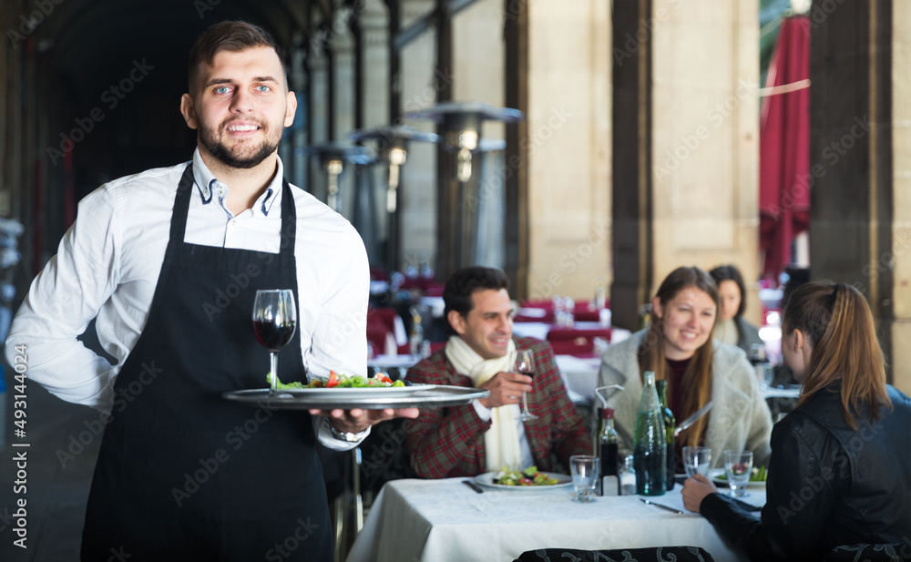 Obraz premium Smiling waiter holding tray at restaurant with customers his behind