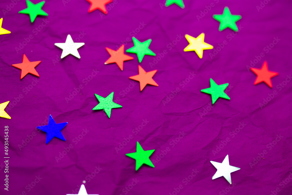 Multicolored bright green, red, blue confetti stars lie on purple background top view. Decor for New year 2022, 2023, Christmas. Abstract backgrounds. Festive sparkles. Birthday, anniversary decor.
