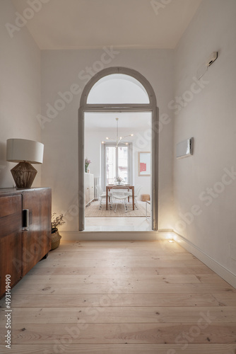 Entrance hall of a house with neo vintage decoration with large wooden lockers, doors with gray semicircular arches and large light pine wood slat floors with a dining table in the background